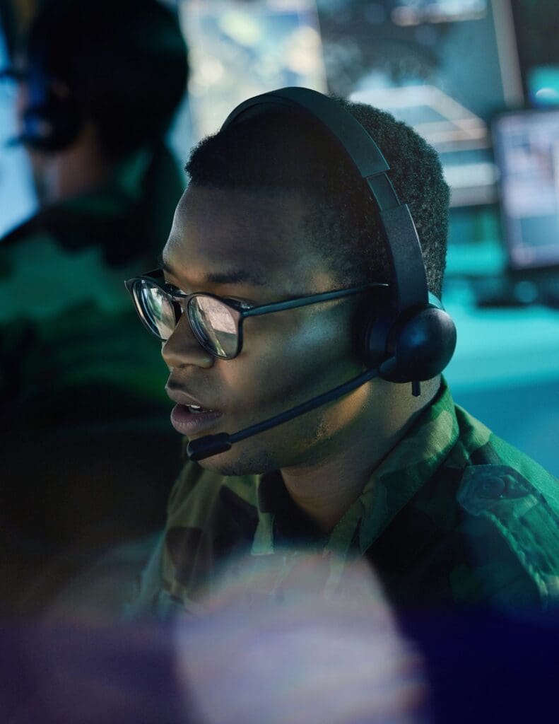 A man in a green camouflage shirt, glasses, and a headset.