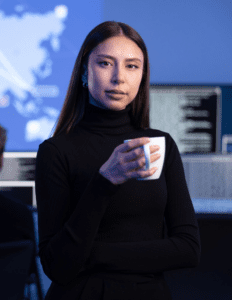 A woman wearing all black smiles while holding a white coffee mug.