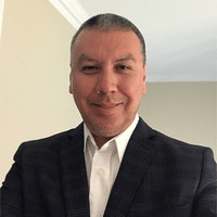 A headshot of a man in a dark blazer and white collared shirt, smiling.