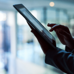 A close-up of a person's hand interacting with a tablet touchscreen in a modern, softly lit office environment.