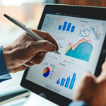 A person points a pen at a tablet displaying various financial graphs and charts, conveying analysis and data-driven decision-making in a professional context.