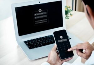 A person uses a smartphone with a numeric keypad to access a laptop displaying a secure login screen. The scene conveys a sense of digital security.