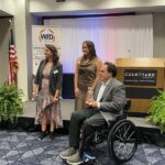 Three people are at an event; Ricardo Romeu holds an award with two applauding.