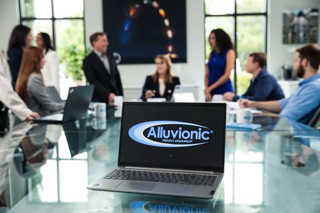 Team members meeting around a conference table with an Alluvionic-branded laptop in the foreground.